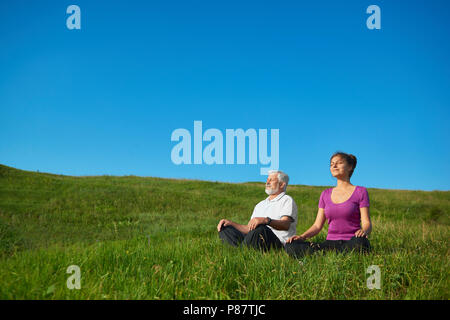 Zwei Menschen meditieren sitzt in das Feld ein. Im Lotussitz auf helle, gesättigte Himmel Hintergrund. Positiv, zufrieden, das gute Gefühl, Konze Stockfoto