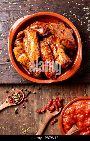 Hohe Betrachtungswinkel von einigen barbecue Chicken Wings in einem Steingut Teller und eine Schüssel mit Barbecue Sauce auf einem rustikalen Holztisch Stockfoto