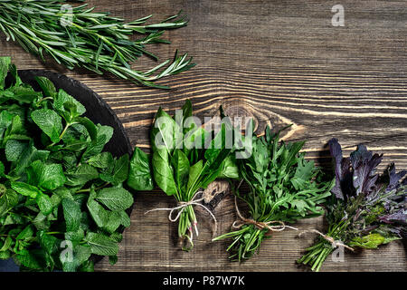 Auswahl an frischen Kräutern auf Holz- Hintergrund. Frisch geerntete Kräuter wie Basilikum, Rucola. Ansicht von oben. Kopieren Sie Platz. Stockfoto