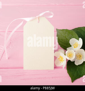 Creme Label mit zarten Jasminblüten auf pastellfarbenen rosa Holz Tisch. Bis Mock, leer Geschenkanhänger. Frühling Sommer Einladung Konzept. Stockfoto