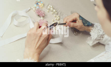 Mädchen Mode Designer Schmuck. Schießen close-up. Sie macht einen Haken auf eine Pin mit künstlichen Perlen. Bänder und künstliche Blumen Stockfoto