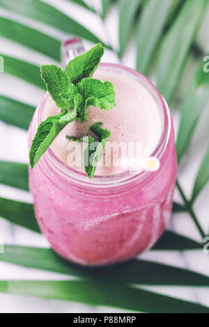 Obst rosa Smoothie in einem Glas auf einem Palm Leaf. Im minimalistischen Stil. Trend vintage getönt. Stockfoto