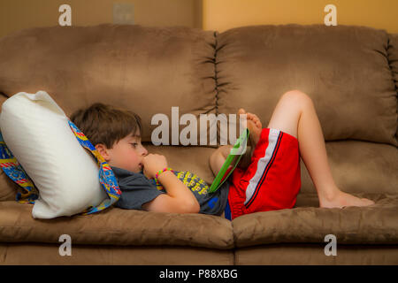 Model Released 9 Jahre alter Junge, entspannend auf der Couch, mit Tablette. Cranbrook, British Columbia, Kanada. Model Release #105 Stockfoto