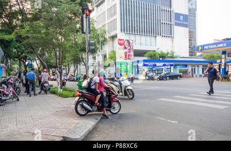 Vietnamesische Mann mit Handy über die Straße und Motorradfahrer mit PKW, Motorrad auf dem Bürgersteig in Ho Chi Minh City, Vietnam. Stockfoto