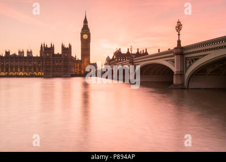 Orange Sonnenuntergang über den Big Ben und die Houses of Parliament in London, einschließlich die Westminster Bridge spiegelt sich in den glatten Wasser der Themse Stockfoto