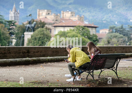 Junges Paar mit Smartphones entspannend auf die alte Stadtmauer von Lucca, Lucca, Toskana, Italien, Europa, Stockfoto