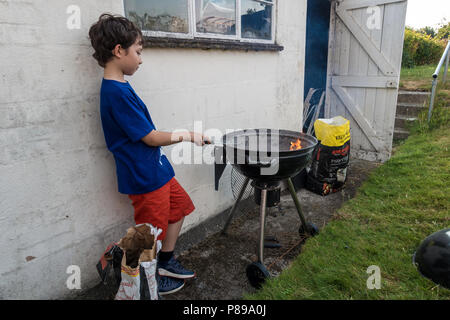 Ein Junge Uhren Flammen als Holzkohle im Grill unten bereit, um Verbrennungen zu kochen. Stockfoto