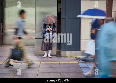 Einen shintoistischen Mönch bittet um Almosen in der Straße in Fukuoka, Japan, durch Bewegung umgeben verschwommen Fußgänger. Stockfoto