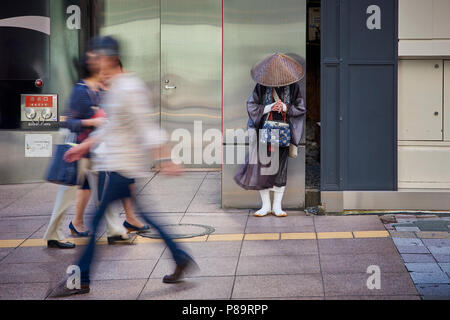 Einen shintoistischen Mönch bittet um Almosen in der Straße in Fukuoka, Japan, durch Bewegung umgeben verschwommen Fußgänger. Stockfoto