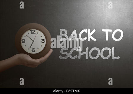 Hand mit der Uhr mit zurück in die Schule Text auf der Tafel Stockfoto