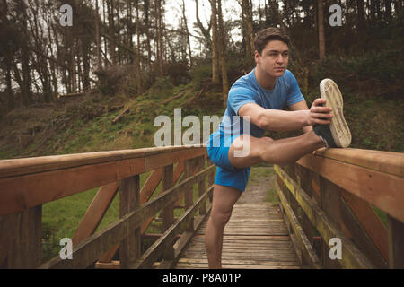 Mann stretching auf hölzernen Brücke im Wald Stockfoto