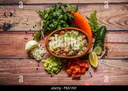 Leckere hausgemachte vegetarische Couscous mit Tomaten, Gurken, Paprika, onoin, Zitrone, Petersilie und Basilikum auf hölzernen Hintergrund, in der Nähe Stockfoto