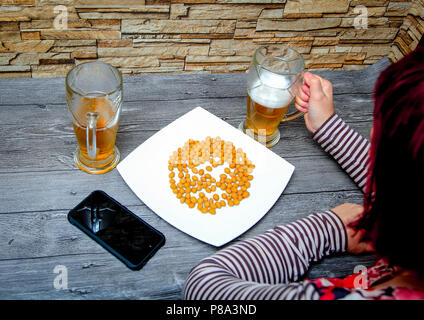 Frau sitzt in einer Bar. Auf dem Tisch sind es wert, zwei Gläser mit Bier, Vorspeisen und liegt Handy. Stockfoto