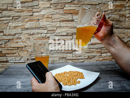 Ein Mann trinkt Bier aus dem Glas in eine Bar und sieht am Handy. Stockfoto