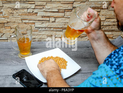 Ein Mann trinkt ein Glas Bier in einer Bar und gesalzene Nüsse isst. Stockfoto