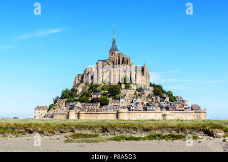 Allgemeine Ansicht des Mont Saint-Michel tidal Island von der Bucht bei Ebbe mit Salz Wiese im Vordergrund unter einem blauen Himmel. Stockfoto