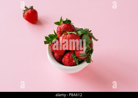 Frische reife Erdbeeren auf einer weißen Schüssel auf einem rosa Hintergrund. Kopieren Sie Platz. Ansicht von oben. Stockfoto