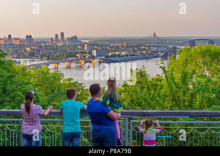 Die Familie schaut auf das Panorama der Stadt mit drei Brücken über den Dnjepr unter das üppige Grün. Kiew. In der Ukraine. Für ihr Design Stockfoto