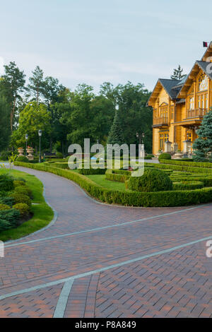 Die Gasse wird mit einem roten Pflastersteinen in einem gut gepflegten Park in der Nähe von einem schönen Holzhaus. Für ihr Design Stockfoto