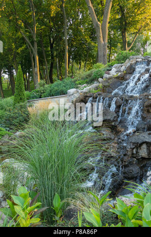 Ein kleiner Wasserfall, der nach unten fließt einem steinigen Hang mitten in einem grünen Park in sonniges Wetter. Ruhe. Für ihr Design Stockfoto