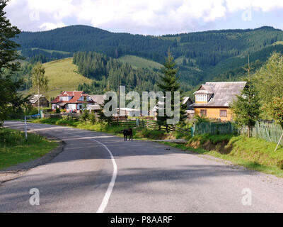 Eine steile Straße mit rustikalen Häusern auf jeder Seite und einen schönen Blick auf den grünen Bergen und dem blauen Himmel. Für ihr Design Stockfoto