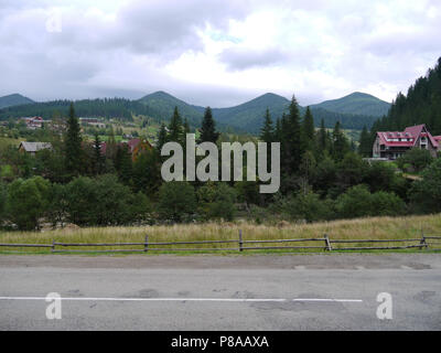 Dorf an der Straße unter den Bergen von grünen Bäumen unter dem bewölkten Himmel umgeben. Ort der Erholung, Tourismus, Picknick. Für ihr Design Stockfoto