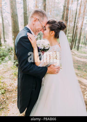 Halbe Länge romantische Porträt des Heiter umarmen Jungvermählten ständigen Kopf-an-Kopf im Wald. Stockfoto