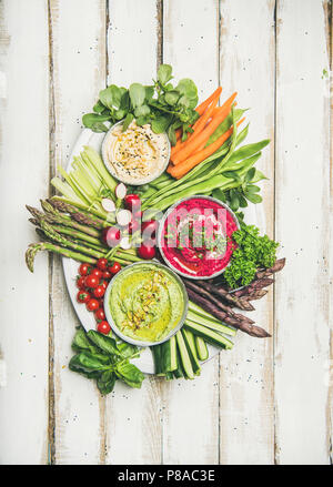 Gesund Sommer veganen Snack plate. Flachbild-lay von Kichererbsen, rote Beete, Spinat Hummus Dips mit frischem Gemüse auf weißem Holz- Hintergrund, Ansicht von oben. Clea Stockfoto