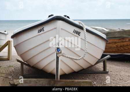 Der Bug eines kleinen weißen Boot namens Annie ruht auf unterstützt in der Nähe der Küste mit dem Meer im Hintergrund in Honiton, Devon, England Stockfoto