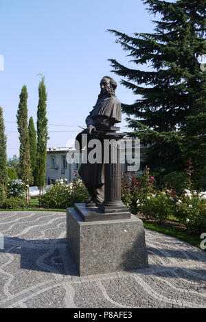 Denkmal für einen Mann aus dem 18. und 19. Jahrhundert auf dem Platz vor dem Gebäude, von blühenden Blumen und hohen grünen Bäumen, unter einem bl umgeben Stockfoto