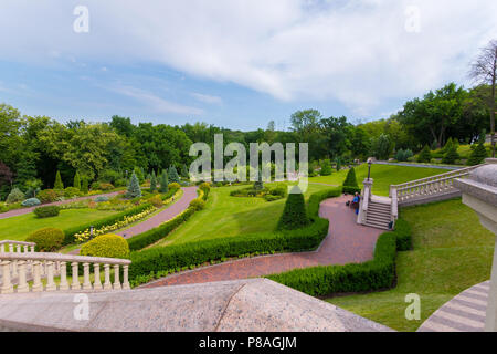 Schritte und Park Pfade durch einen grünen Rasen, Blumenbeeten, Fichte von hohen grünen Bäumen, unter einem blauen bewölkten Himmel umgeben. Für ihr Design Stockfoto