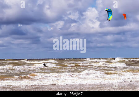 Zwei Kitesurfer Reiten die Wellen der Ostsee in der Nähe von Venspils Strand unter den bewölkten Himmel. Spaß im Meer. Extreme Sport Kitesurfen. Stockfoto