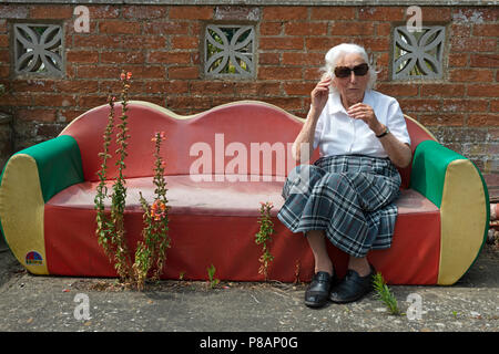 Ältere englische Lady auf einem Garten sofa während der langen heißen Sommer 2018 Stockfoto