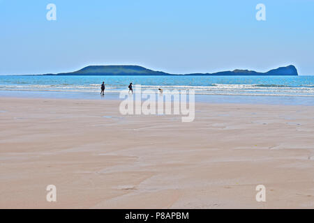 Ein paar Urlauber zu Fuß ihren Hund entlang der Küste am Strand von Llangennith gegen Würmer Kopf, Rhossili Bay, Gower, s. Wales Stockfoto