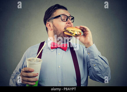 Übergewicht business Mann essen mit Appetit ein Burger Holding eine große Dose Soda drink Stockfoto