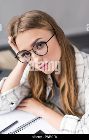 Schön müde studert Mädchen mit Notebook sitzen am Arbeitsplatz und suchen an Kamera Stockfoto