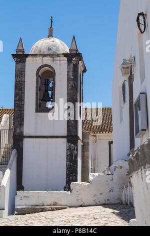 Turm von a Nossa Senhora de Assuncao Kirche. Seitliche Sicht auf den Glockenturm mit einer Glocke. Schwarze Steine Kanten eines weißen Gebäude. strahlend blauen Himmel. Cacela Velha Stockfoto