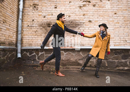 Nette junge Paare halten sich an den Händen und laufen neben dem alten Gebäude Stockfoto