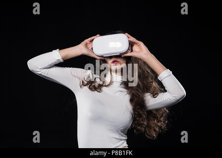 Attraktive brünette Frau mit Virtual reality Headset isoliert auf Schwarz Stockfoto