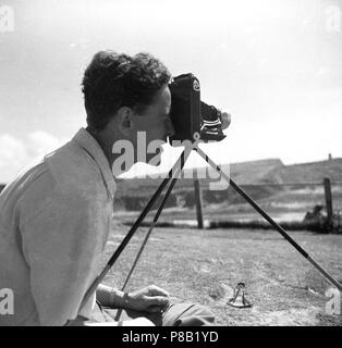 1950, historische, Mann ein Foto außerhalb mit einem klappbaren Film Kamera auf einem Stativ, England, UK. Bild zeigt die Kamera in Ausklappen. Solche Kameras waren sehr beliebt, mit begeisterter Amateur, da sie mobil im Vergleich zu größeren, schwereren Kameras waren aber immer noch ein Film, ein größeres Filmformat, (6 x 9), daher die Gewinnung qualitativ bessere Fotos. Stockfoto