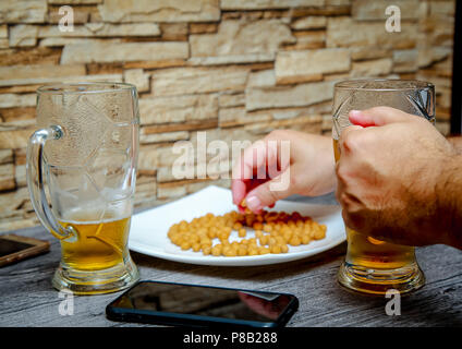 In der Nähe der Männer Hände halten ein Glas Bier und die Muttern von der Platte. Stockfoto