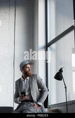 Unternehmer im Baseball Cap holding Smartphone und Wegsehen Stockfoto