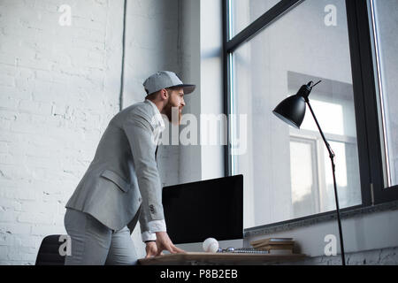 Unternehmer im Baseball Kappe am Fenster im Büro Stockfoto
