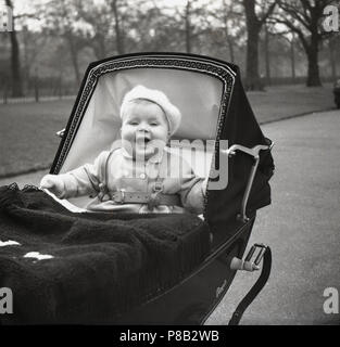 1950er Jahre, Kind in Kleidung und tragen eine Beere auf ihren Kopf in ihren coachbuit Royale luxus Kinderwagen sitzen mit einem grossen Lächeln auf ihrem Gesicht chirpy, England, UK. Stockfoto