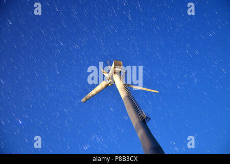 Ansicht von unten eines beschädigten drei Blade Windkraftanlage Windmühle über klaren, blauen Nachthimmel mit star Trails. Stockfoto