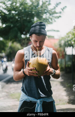 Schöner Mann trinken Kokosnuss Wasser im Tropical Resort in Bali, Indonesien Stockfoto