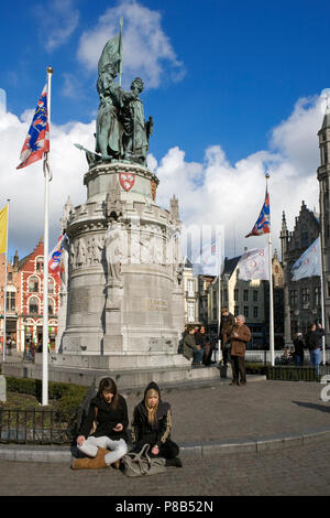 Zwei Mädchen sitzen am Fuße der heroische Statue von Jan Breydel und Pieter De Coninck im Markt, Brügge, Belgien Stockfoto