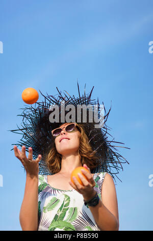 Ansicht von unten auf das schöne junge Frau in hat das Jonglieren mit Orangen gegen den blauen Himmel Stockfoto