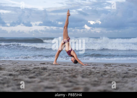 Seitenansicht der sportliche junge Frau Yoga in einem vierbeinigen Downward-Facing Hund darstellen (Eka Pada Adho Mukha Svanasana) an der Küste Stockfoto