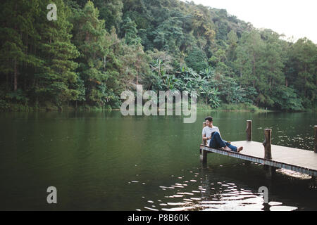 Ein Mann sitzen entspannt auf Holzbrücke am Lakeside am Nachmittag. Stockfoto